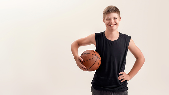 Portrait of cheerful disabled boy with Down syndrome smiling at camera while posing with basketball isolated over white background. Front view. Web Banner