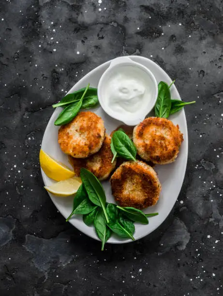 Tuna and potato cutlets with spinach and greek yogurt on a dark background, top view