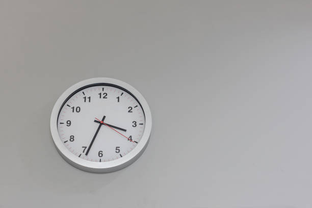 istock Big clock hanging on grey wall. Classic round wall clock on the grey background. Round clock on office wall 1290089267
