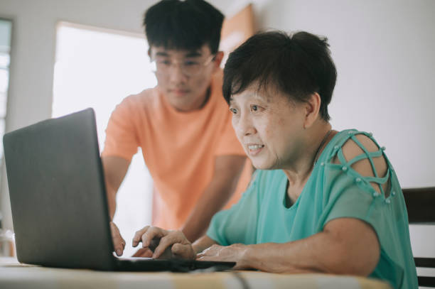 an asian chinese senior woman learning how to use laptop for social media from her grandson at dining room - grandparent using computer laptop dining table imagens e fotografias de stock