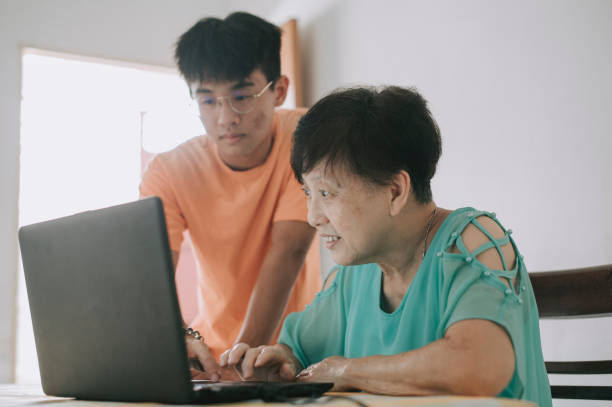 azjatycka chińska starsza kobieta uczy się, jak używać laptopa do mediów społecznościowych od wnuka w jadalni - grandparent using computer laptop dining table zdjęcia i obrazy z banku zdjęć