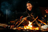 キャンプの火の周りに座って、冬の夜に食べ物や飲み物を楽しむ友人のグループの中で若い女性の肖像画