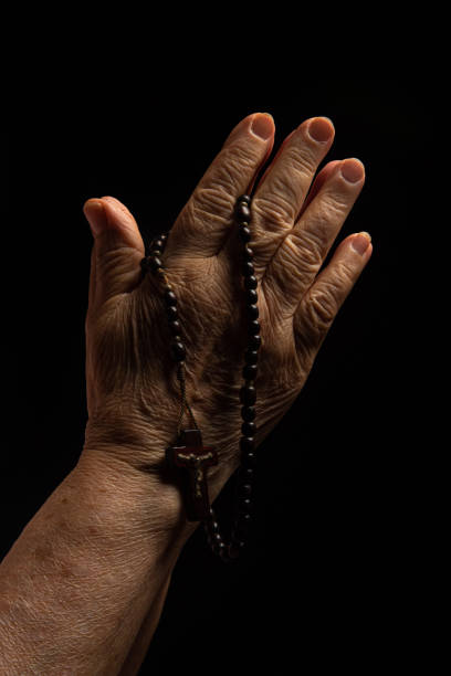 istock Faith, lady's hands with a third praying over black background, selective focus. 1290093722
