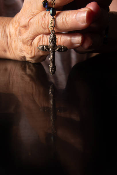 istock Faith, lady's hands with a third praying over black reflective surface, selective focus. 1290095281