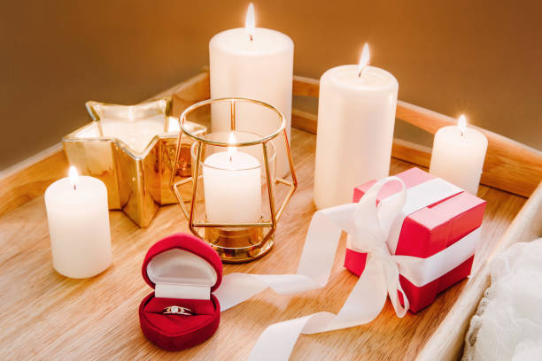 istock Proposal, engagement concept. Red box with gold engagement ring and gift box on background of burning candles. Romantic dinner. Selective focus. 1290095974
