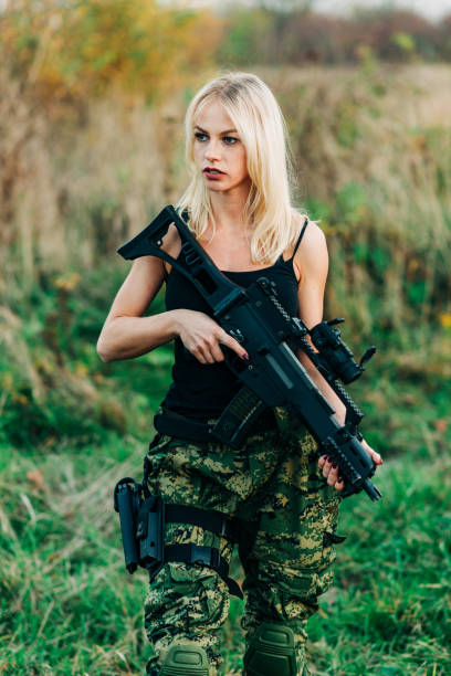 istock Blonde girl posing with an automatic rifle. 1290101678