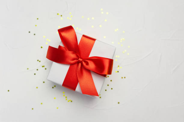 istock Decorative white gift box with a large red bow on white background with golden little stars. Greeting card template with place for text 1290102866