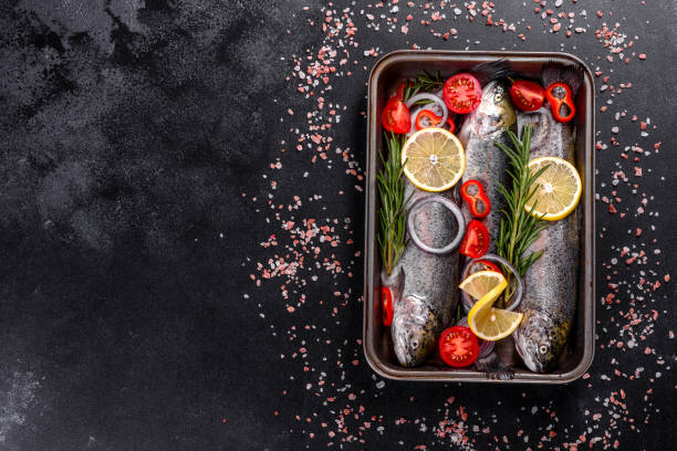 istock Raw trout lie on a black stone chopping board on a dark concrete table 1290104898