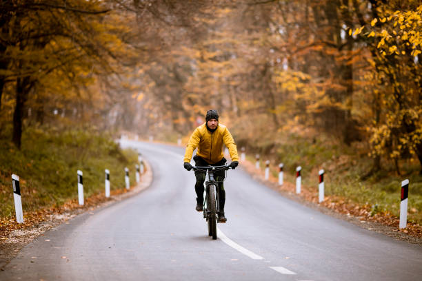 istock Young man biking on a country road through autumn forest 1290105320