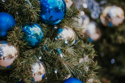 Close up of Christmas tree branch decorated with blue and silver ornaments, string lights and giant snow flakes. Winter holiday card with copy space.