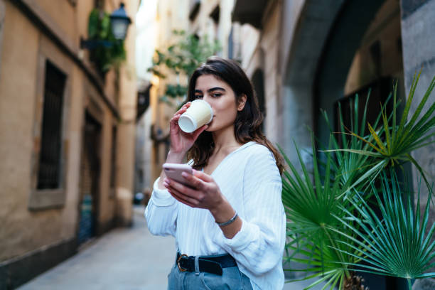 istock Stylish woman drinking coffee with smartphone in hand 1290106542
