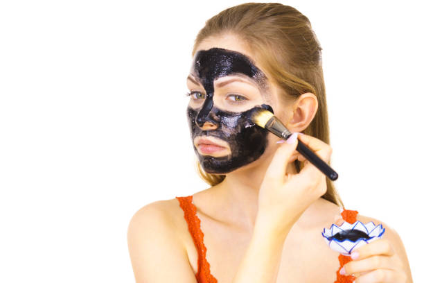 istock Woman applying black mask to skin face 1290106821