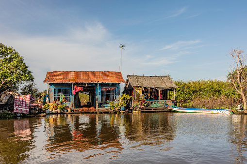 Typical Floating homes in the Mechrey Floating Village. These homes have fishing nets on the front decks and a long-tail boat tied to the deck. The boat is used for fishing and transportation.