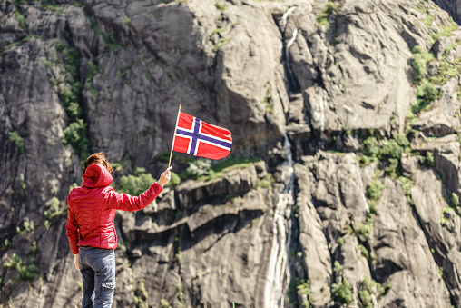 Tourist woman with norwegian flag in rocky stone mountains.