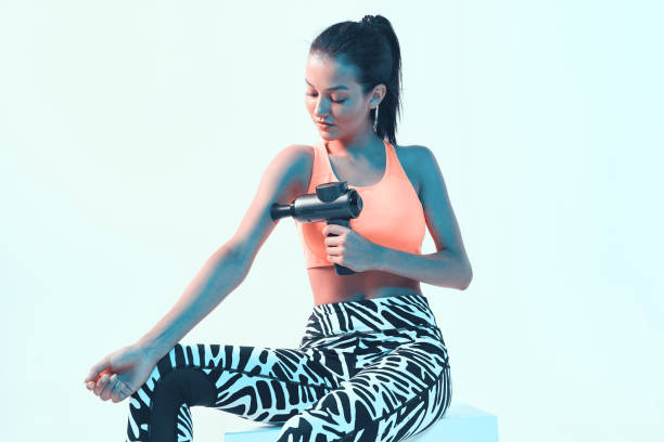 istock Athletic young brunette female massaging hand by handheld percussion massager in neon light 1290112930