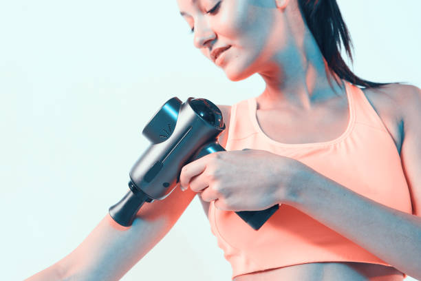 istock Athletic young brunette female massaging hand by handheld percussion massager in neon light, close up 1290113914