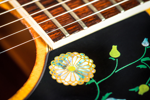 Close-up showing the end of the fretboard meeting the soundhole on a vintage acoustic guitar, with an inlaid flower decoration on the pickguard.