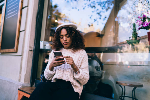 istock Pensive dark skinned curly woman using smartphone for reading messages and checking notification on smartphone, beautiful african american female influencer watching videos from social networks 1290123908