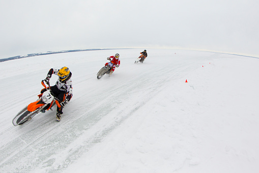 Two men lead a woman through a corner during a winter motorcycle ice race on Gull Lake in Alberta, Canada. Their tires have metal studs for grip on the snow and ice. (John Gibson Photo/GibsonPictures)