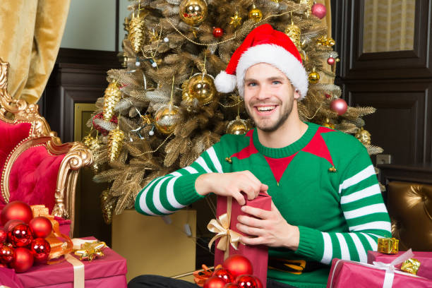 istock Man in santa hat smile with presents at Christmas tree 1290128196