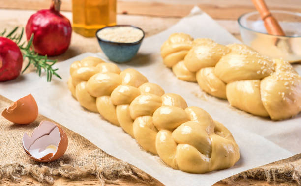 challah brot vor dem backen. proofing süße brötchen mit sesamsamen auf pergament bestreut. granatapfel, eierschalen und butter für brot auf dem tisch. nahaufnahme, produktlayout - hanukkah loaf of bread food bread stock-fotos und bilder