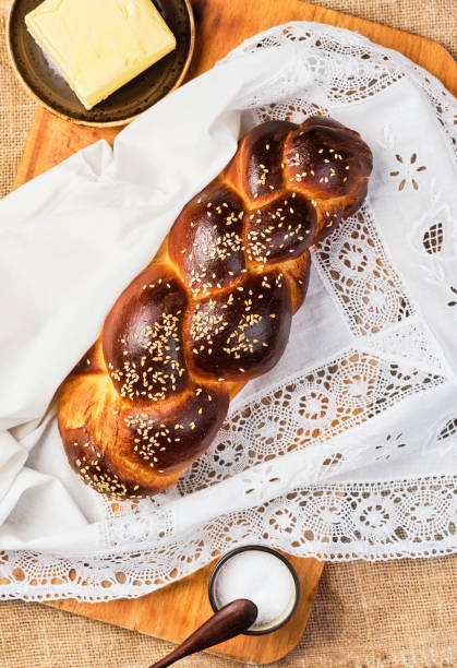 frische hausgemachte challah mit sesamsamen auf einer weißen spitzenserviette. salz und butter auf dem tisch. top-ansicht, challah für samstag - hanukkah loaf of bread food bread stock-fotos und bilder