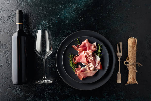Prosciutto and rosemary on a black plate.