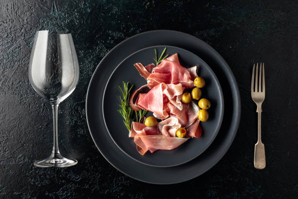 istock Prosciutto, green olives and rosemary on a black plate. 1290131663