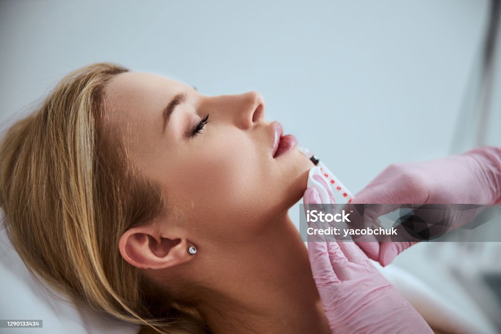 Professional cosmetologist injecting a dermal filler into the patient lips Side view of a woman undergoing the lip augmentation procedure done in a beauty salon Dermal Filler Stock Photo