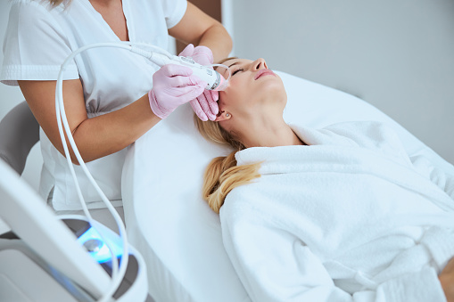 Professional Caucasian dermatologist conducting a microneedling procedure on her young patient using a modern beauty device