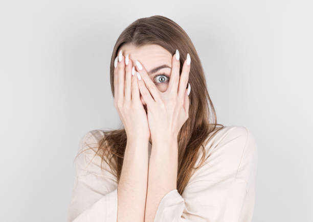 istock Beautiful caucasian young female peeks though fingers, covers face with both hands, isolated over white background. 1290134109