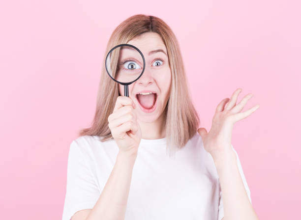istock Young attractive blonde woman shocked while looking through a magnifying glass over pink background. 1290134111