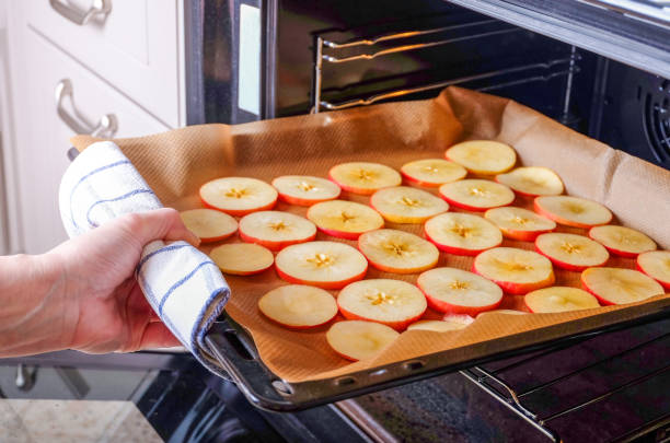 une femme au foyer met une plaque à pâtisserie de pommes tranchées dans un four électrique pour sécher. - dried apple photos et images de collection