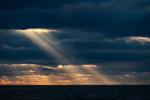 Sunbeam over a dark sea through dark clouds