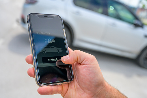 Unlocking passenger car just by tapping on display. Male hand using smartphone with car unlock software. Wireless, modern technology concept.