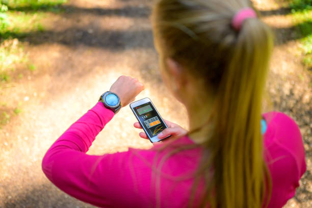 vue à angle élevé sur la femme utilisant le logiciel de traqueur sur le smartphone et la montre intelligente - medical cross photos et images de collection