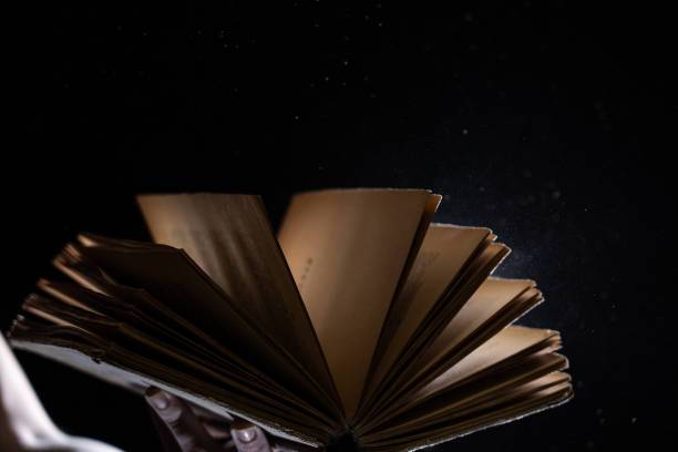 istock Hand holds Vintage open Book Glows on black background. Concept of reading, knowledge and open mind 1290148882