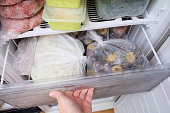 A hand opening a drawer of a freezer with frozen foods, long-term food storage and inventory at home