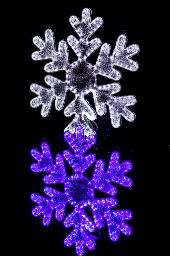White and purple snowflakes as a part of holiday outdoor lighting decorations, close-up on the black night background