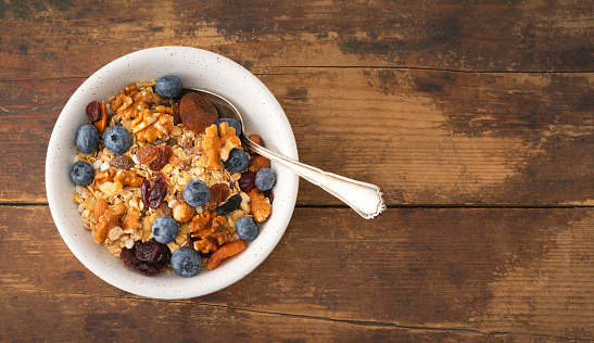 A healthy oatmeal for breakfast, with fresh organic fruit, banana and blueberry, nuts and grains, at a wooden table in a modern white kitchen, representing a healthy lifestyle and wellbeing, an image with a copy space