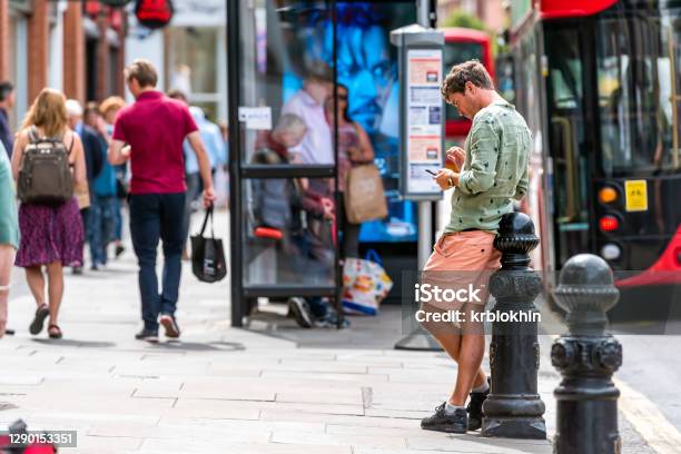 Young Man Browsing Using Phone On Sidewalk Street By Double Decker Bus Stop With People In Chelsea Stock Photo - Download Image Now