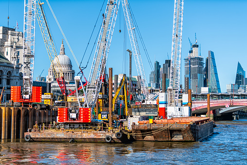 London, UK - June 22, 2018: Cityscape of Thames River construction for clean-up with cranes at ship port wharf by skyline of skyscrapers and Blackfriars bridge and St. Paul's cathedral church