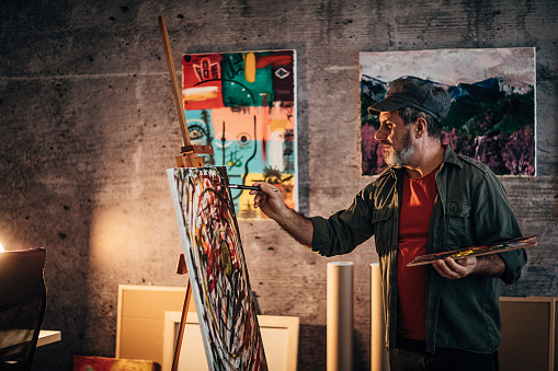 One senior man, painter, painting on a canvas late into the night in his home studio.