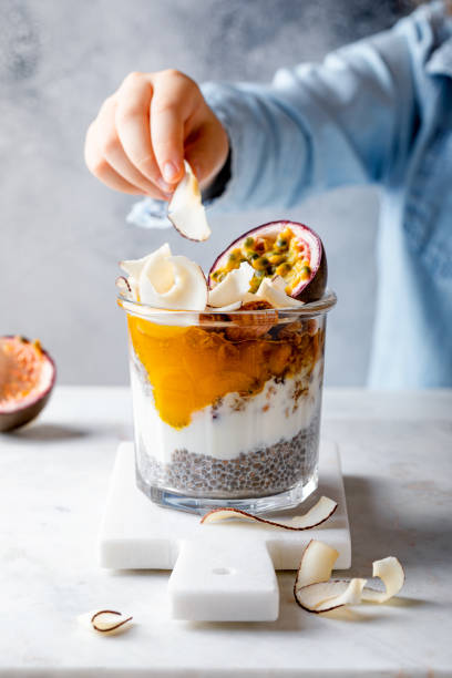 Healthy tropical fruit chia pudding with granola, mango, passion fruit and coconut chips in a glass jar. Vegan healthy breakfast, clean eating. Little girl eating healthy tropical fruit chia pudding with granola, mango, passion fruit and coconut chips in a glass jar. Vegan healthy breakfast, clean eating. eating chia seeds stock pictures, royalty-free photos & images
