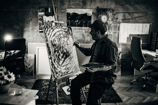 One senior man, painter, painting on a canvas late into the night in his home studio.
