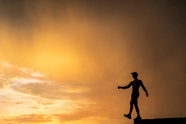 istock Silhouette of Man stepping from the edge during dramatic sunset. Concept goal, step forward and risk 1290166543