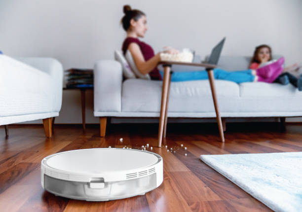 A woman and her daughter eating popcorns while a robotic vacuum cleaner working stock photo