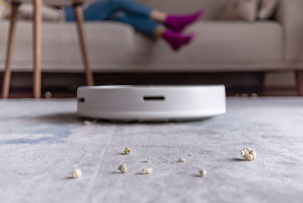 Close-up shoot of a woman relaxing and eating popcorns while a robotic vacuum cleaner working stock photo