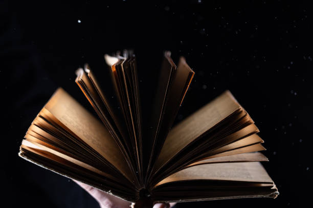 istock Hand holds Vintage open Book Glows on black background. Concept of reading, knowledge and open mind 1290174746