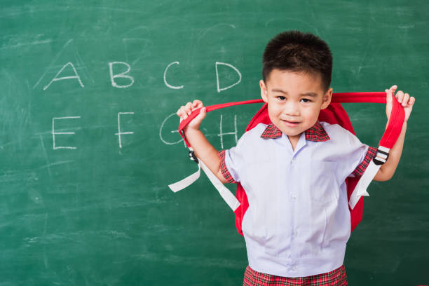 istock child boy from kindergarten in student uniform with school bag stand smiling on school blackboard 1290189551